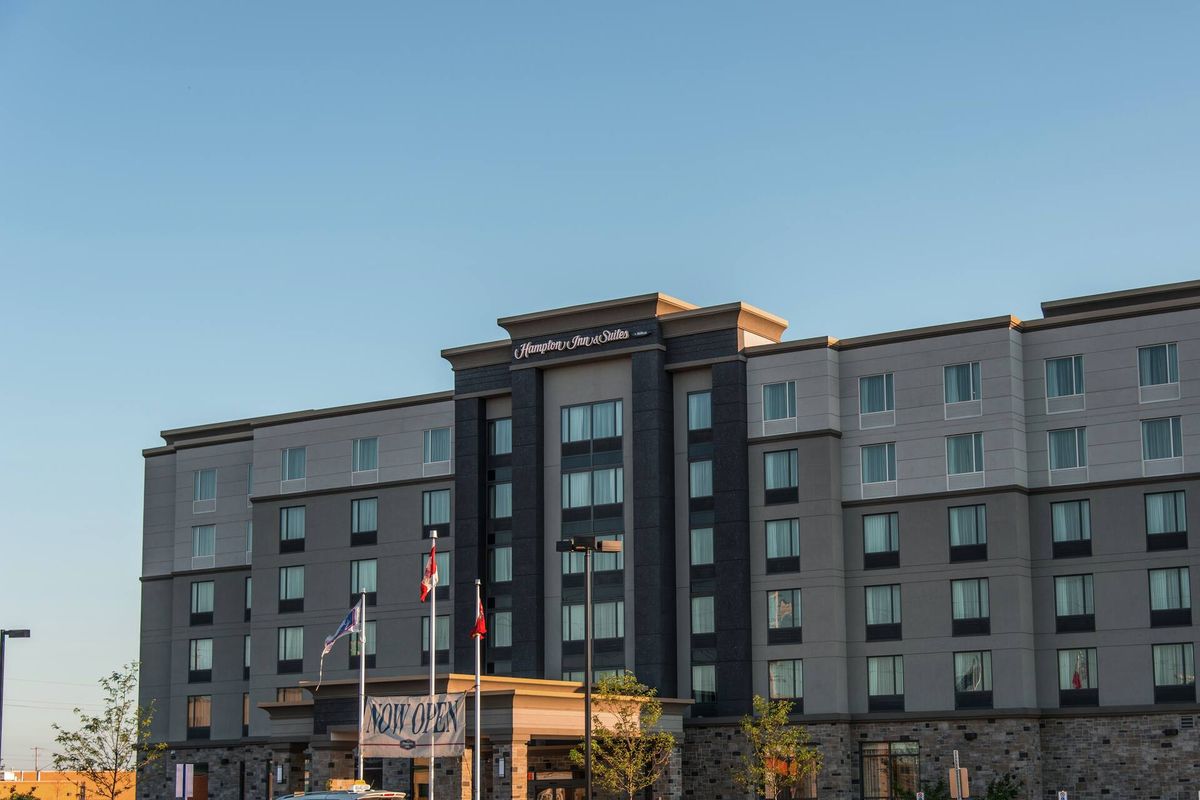 Exterior of Hampton Inn & Suites by Hilton Bolton, a grey and stone hotel with flags at the entrance